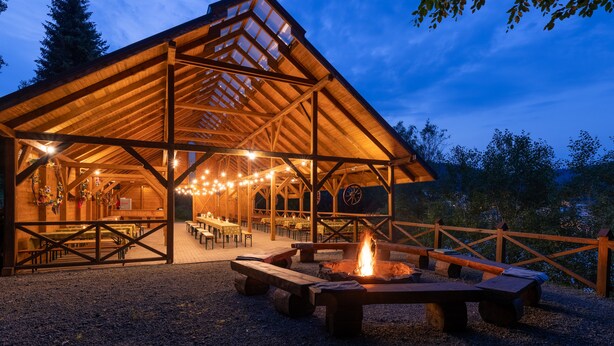 A wooden pavilion with a covered dining area, outdoor seating, and a central fire pit. - Hotel Krynica Conference & SPA (Krynica-Zdroj)