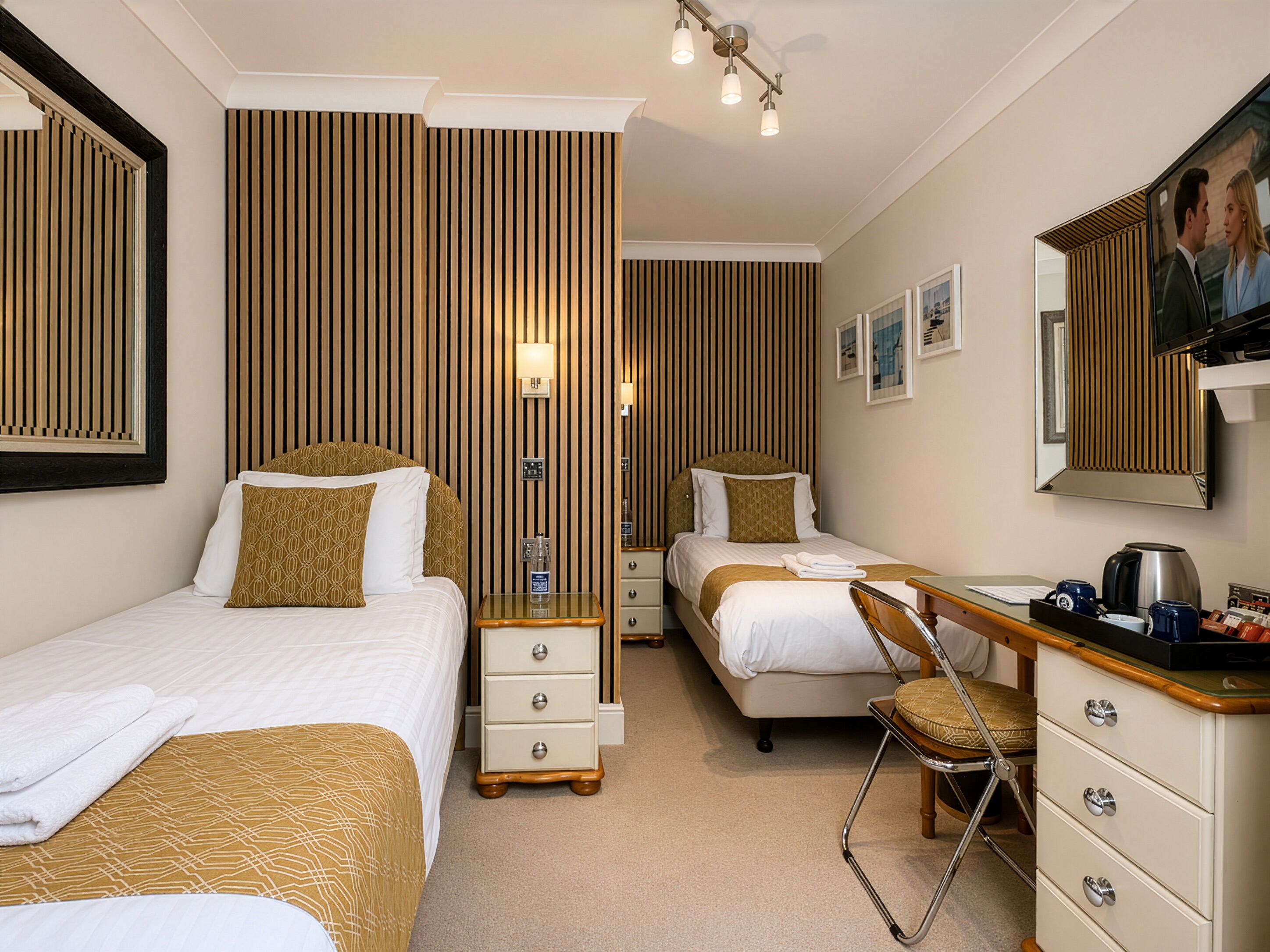 Une chambre d’hôtel avec deux lits, un bureau, une chaise, une commode, un miroir et un téléviseur.