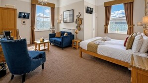 Een hotelkamer met een bed, een blauwe fauteuil, een bank, een bureau en uitzicht buiten.