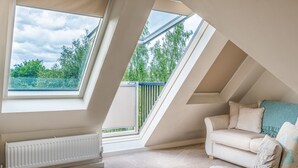 Habitación con techo inclinado, un radiador, un sofá color beige y vistas a la vegetación a través de tragaluces.