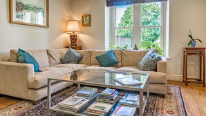 Una sala de estar con un sofá color beige, una mesa de centro de vidrio y un tapete estampado.
