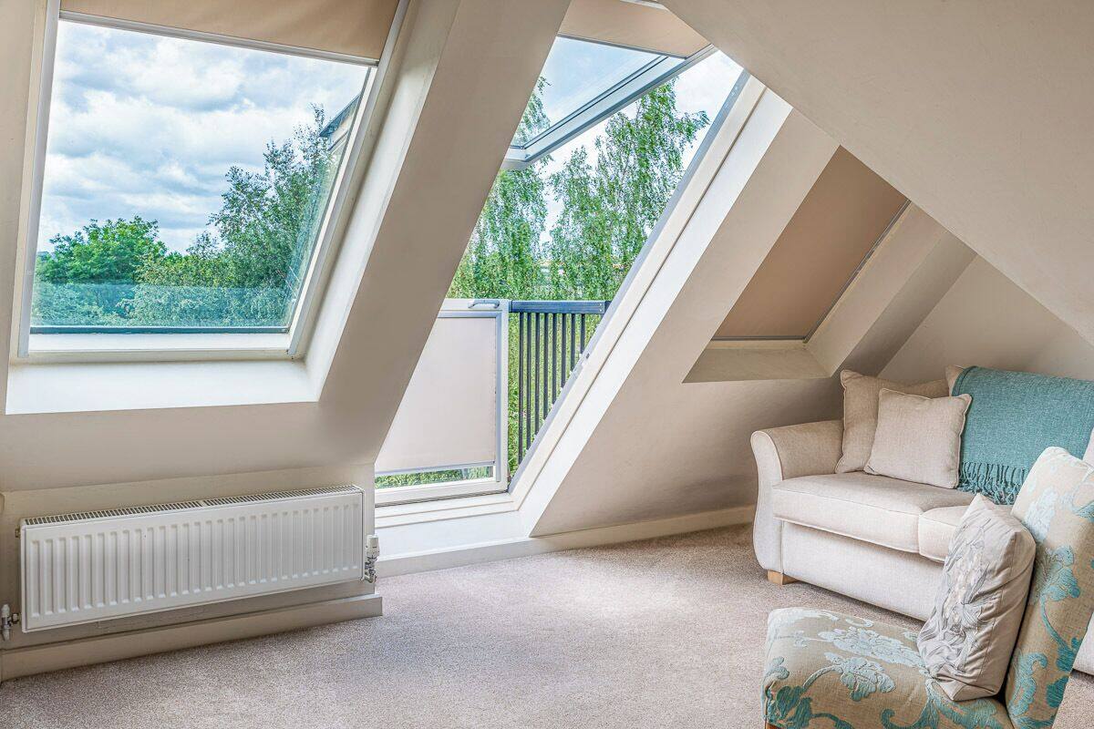 A room with a sloped ceiling, a radiator, a beige sofa, and a view of greenery through skylights.