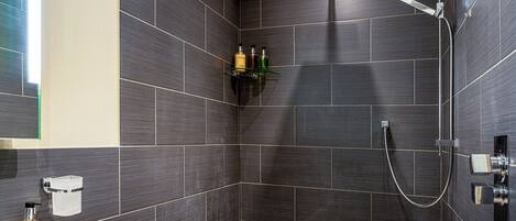 Ein modernes Badezimmer mit dunklen Fliesen, einer Dusche und einem Ablagefach für Pflegeprodukte.