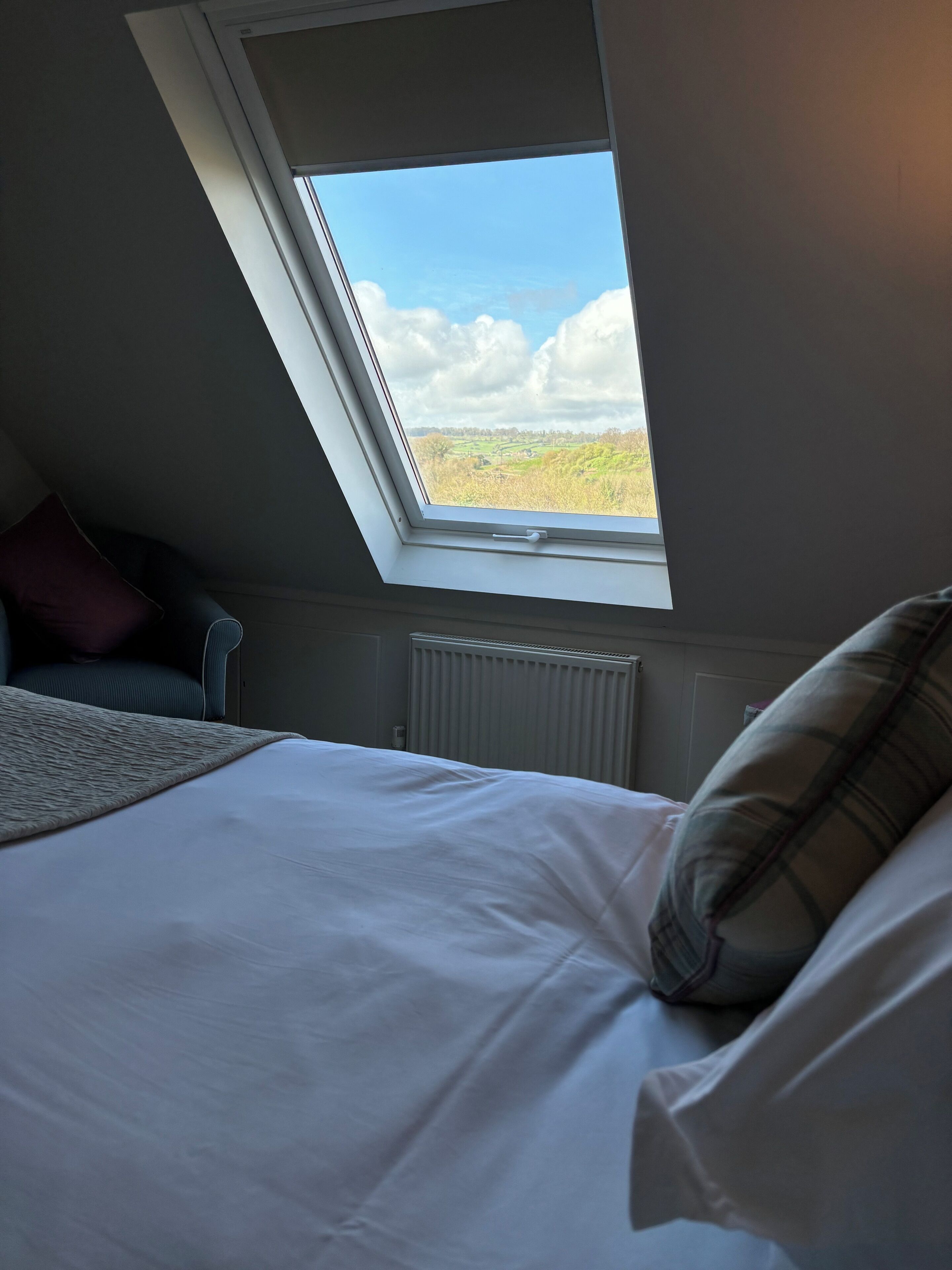 Ein Schlafzimmer mit Dachfenster, einem Bett, einer Heizung und Blick ins Grüne.