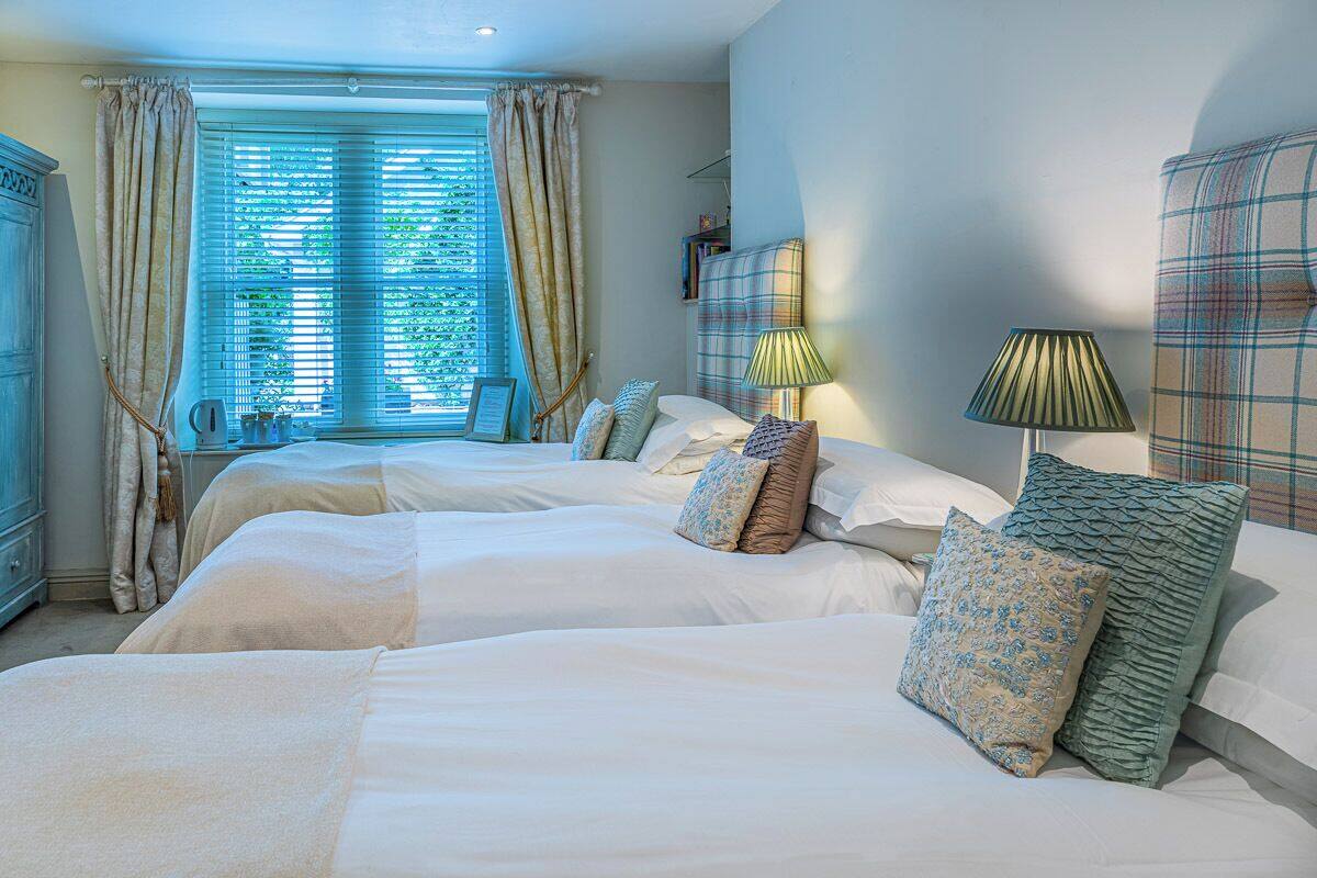 A bedroom with two beds, a window with curtains, a bedside table with lamps, and a wardrobe.
