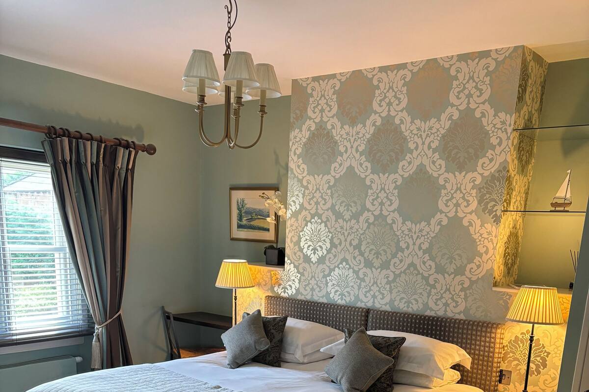 A bedroom with a large bed, two bedside tables, a chandelier, and patterned wallpaper.