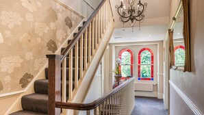 Una escalera con barandilla de madera, peldaños alfombrados y papel tapiz con motivos florales.