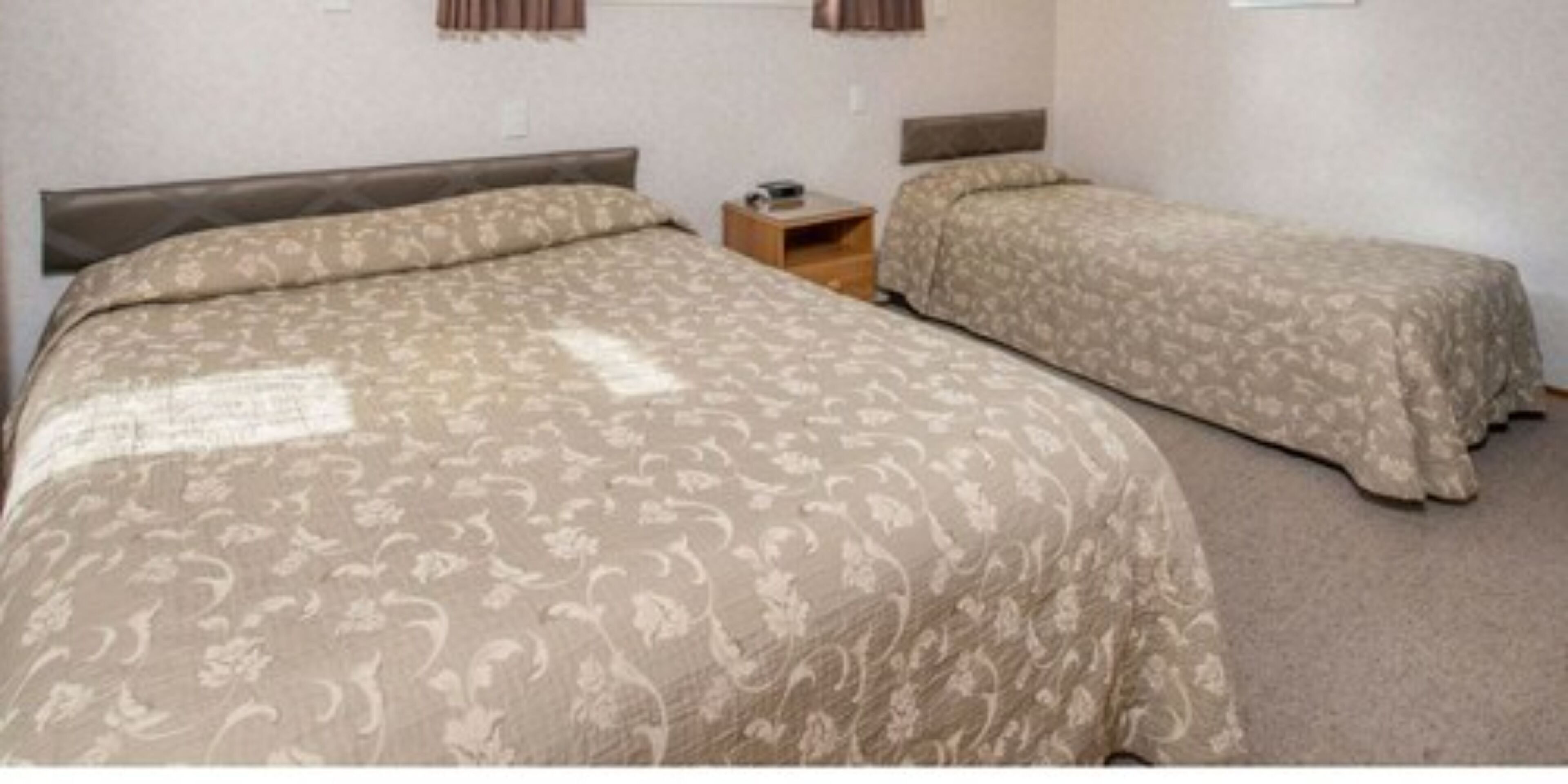 Una habitación con una cama grande y dos camas más pequeñas. Hay una mesita de noche con una lámpara y una pequeña mesa.
