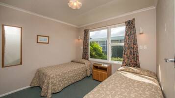 A room with two single beds, a small wooden cabinet, a window with curtains, and a framed picture on the wall.