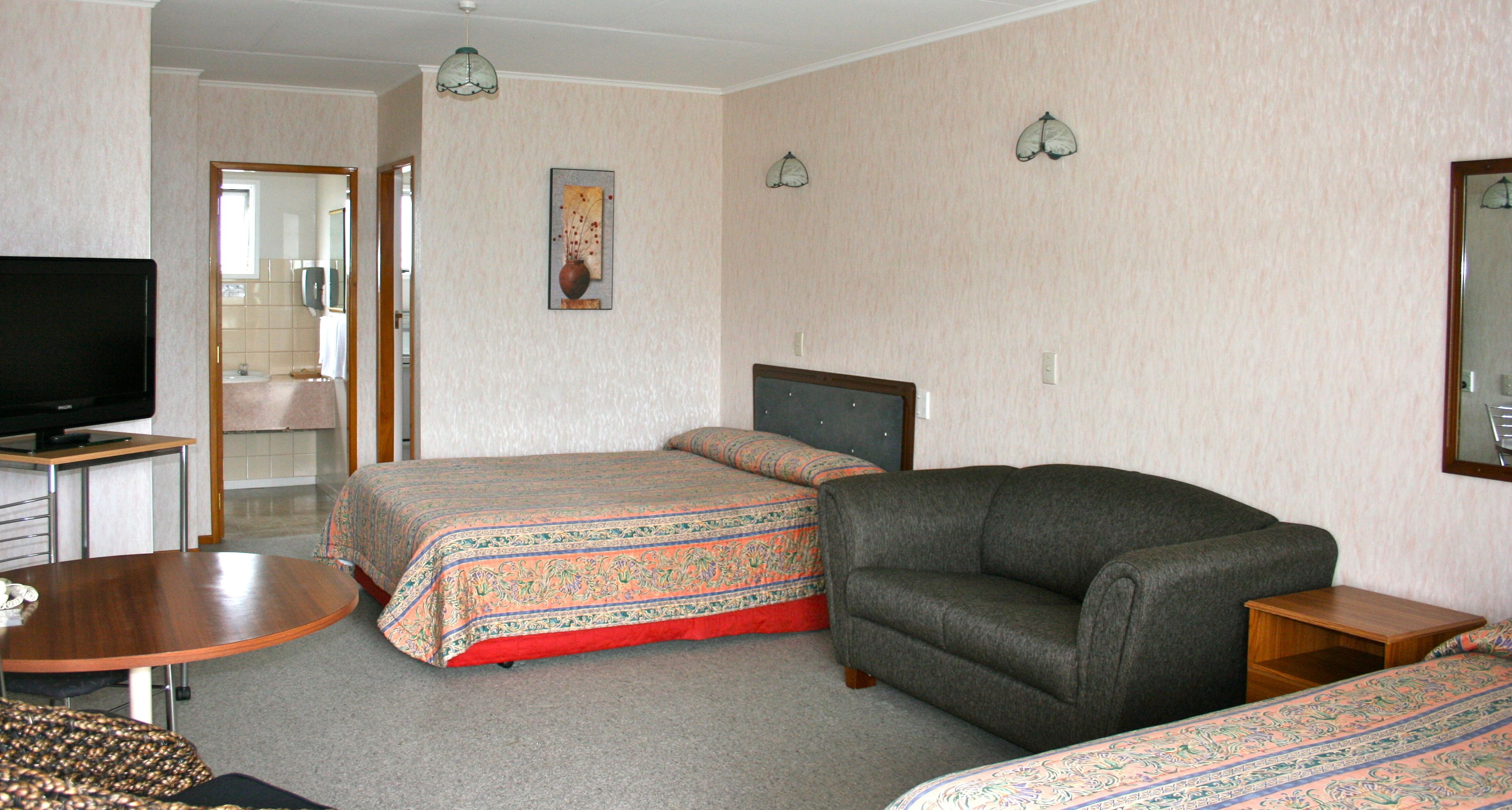 A hotel room with two beds, a sofa, a TV, and a small table.