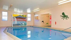 En indendørs swimmingpool med en blå vandoverflade, et springbræt og en teltformet struktur i baggrunden.