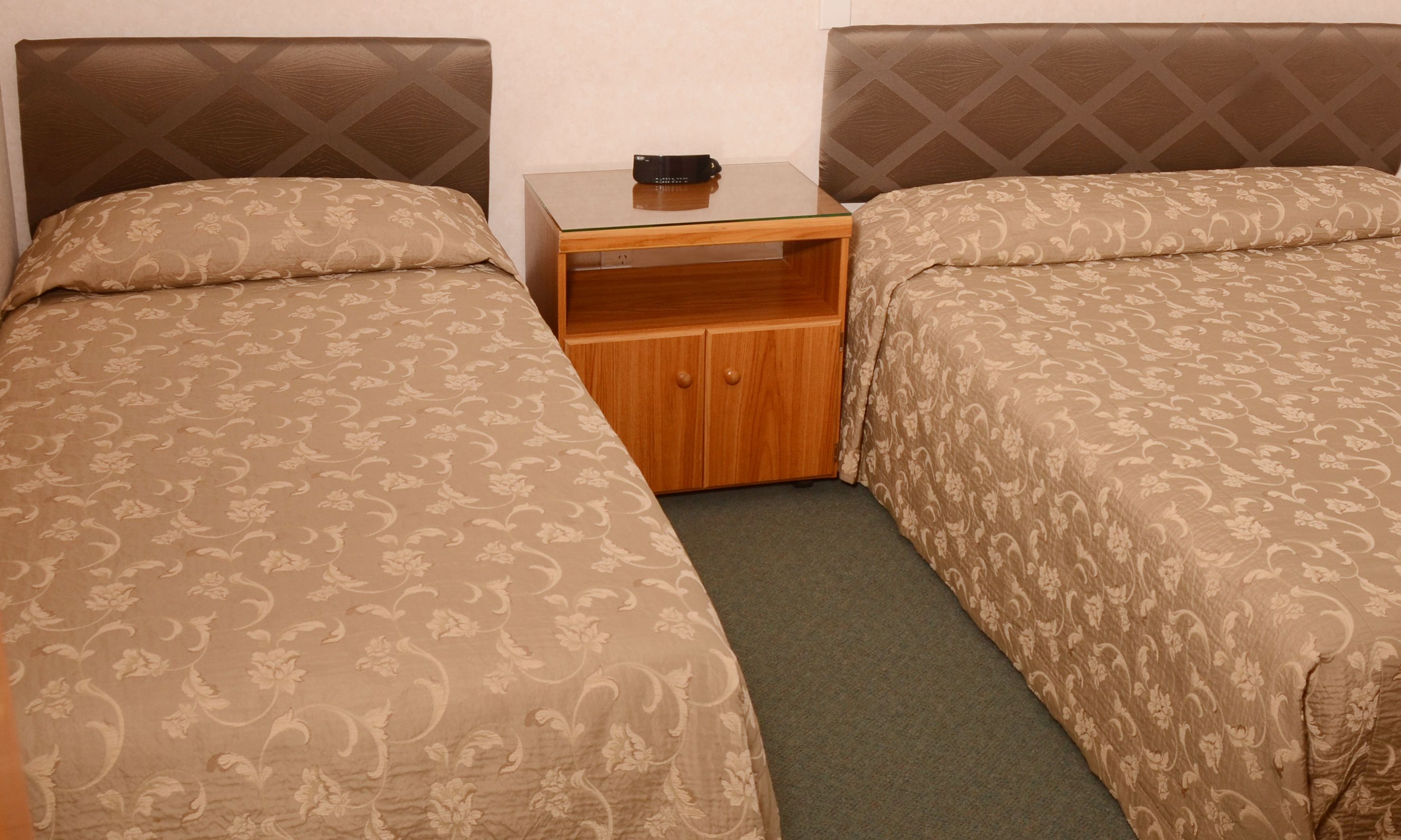 Quarto duplo com duas camas, uma mesa de cabeceira de madeira e uma pequena mesa.