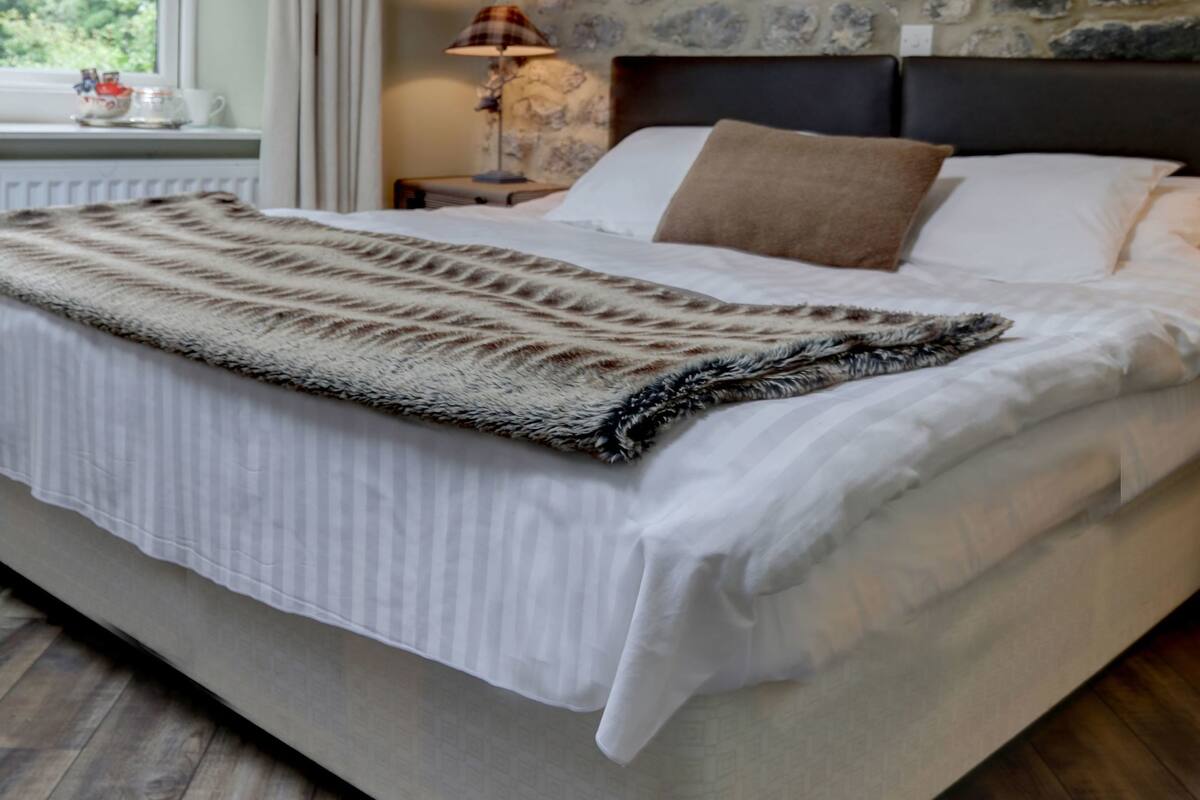 Quarto com uma cama grande, parede de pedra, lustre e janela com cortinas.