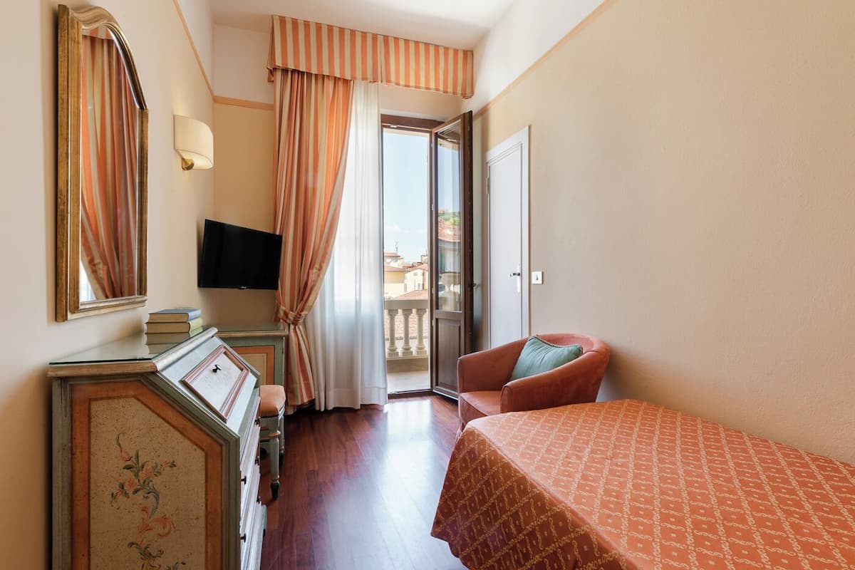 A hotel room with a bed, a chair, a TV, a dresser, and a view of the outside.