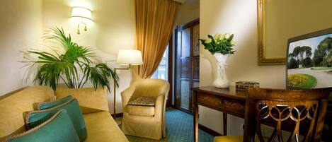 A hotel room with a sofa, armchair, dining table, and a large mirror.