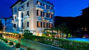 A multi-story hotel with a pool, surrounded by greenery and a well-lit exterior. - Hotel Parma e Oriente Wellness & Spa (Montecatini Terme)