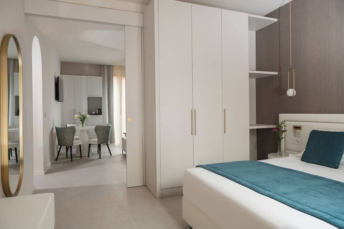 A modern bedroom with a bed, a desk, and a chair. There is a wardrobe with two doors and a mirror.
