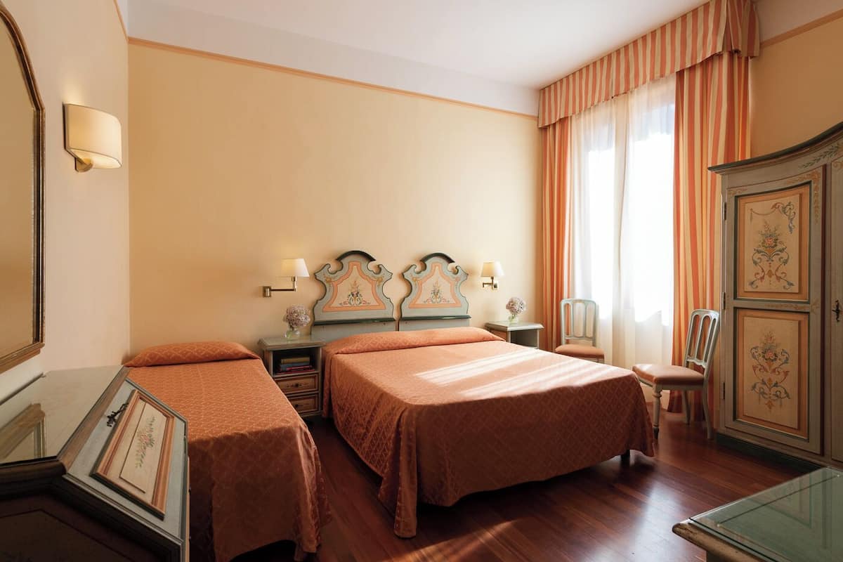 A hotel room with two beds, a dresser, a chair, and a mirror.