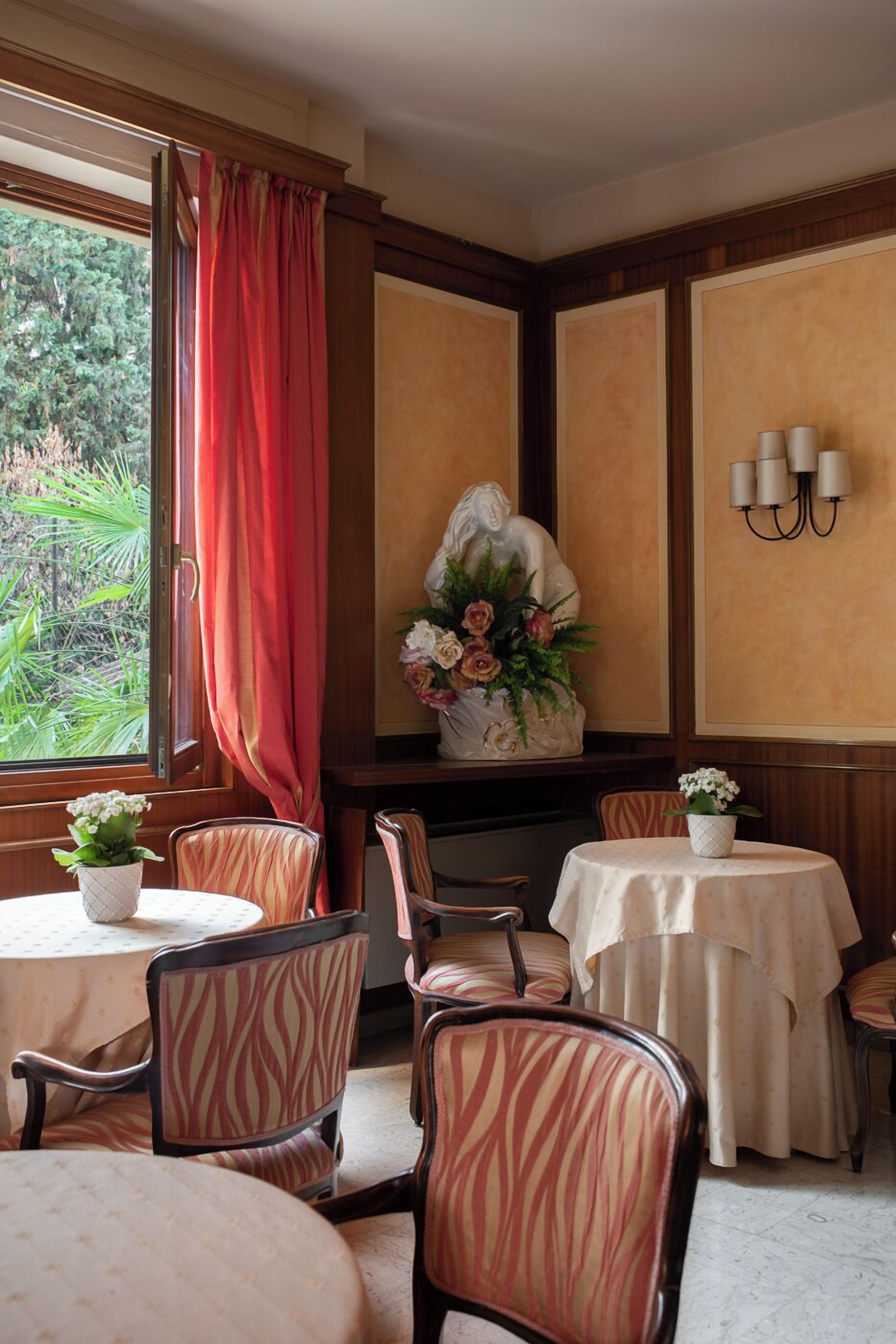 A dining area with a table set for four, a vase with flowers, and a window with red curtains.