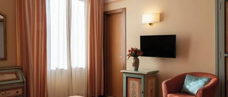 Et hotelværelse med en seng, et fjernsyn hængt på væggen, et lille skab med en vase med blomster og en stol.
