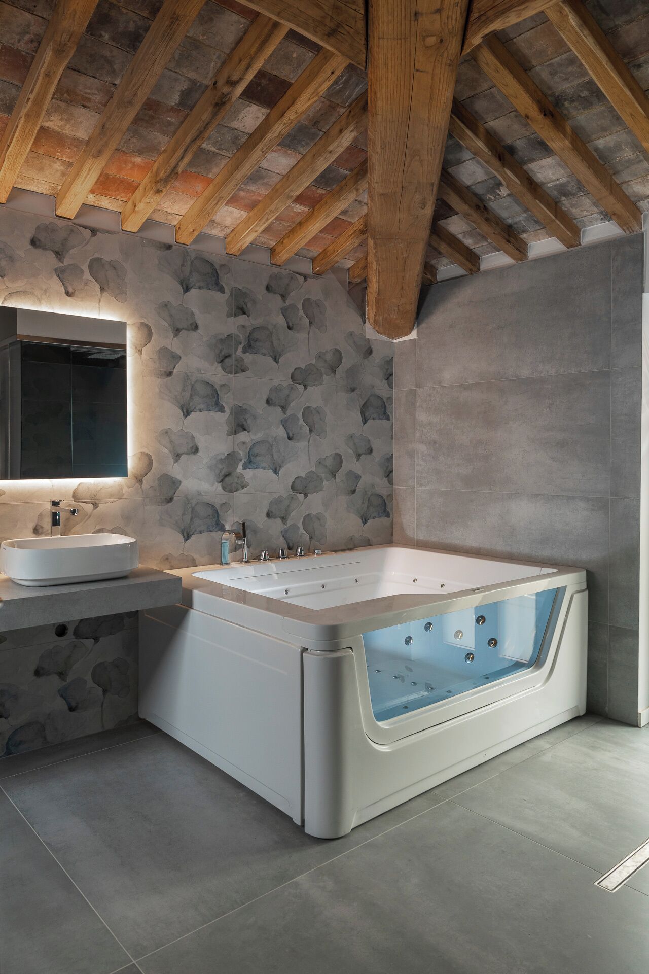 A modern bathroom with a stone-patterned wall, a freestanding bathtub, and a large mirror above the sink.
