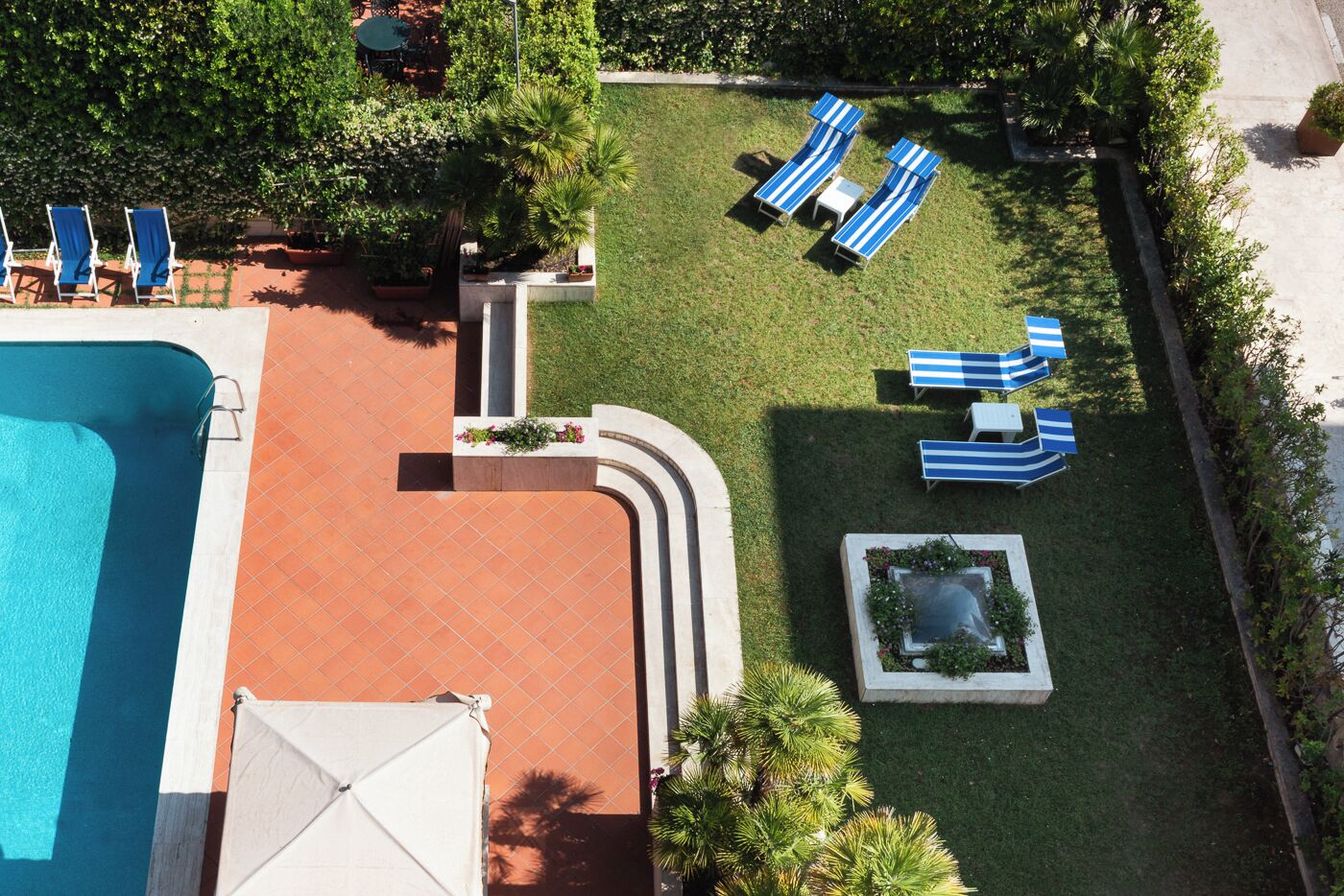An aerial view of a resort with a swimming pool, lounge chairs, and a well-maintained lawn.