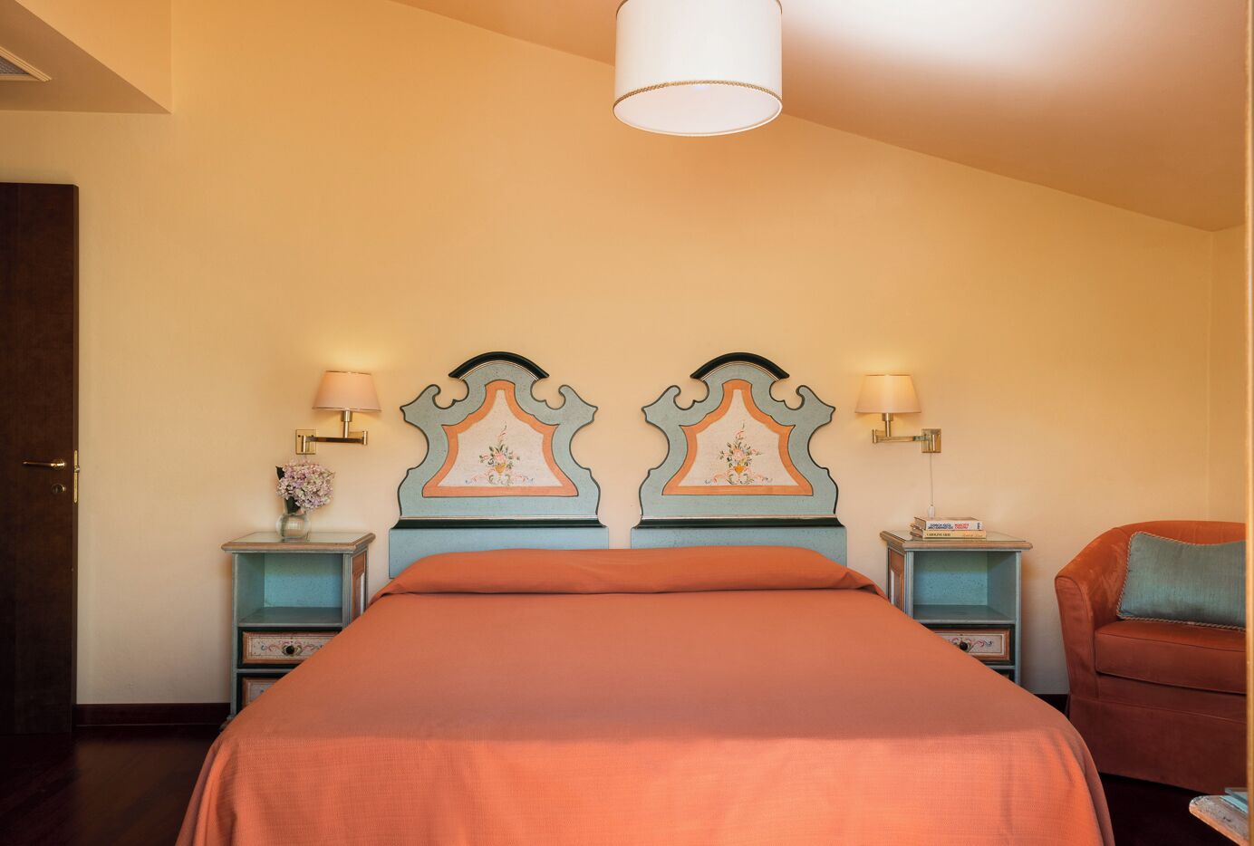 Habitación de hotel con una cama grande, dos mesitas de noche, una silla y una lámpara en el techo.