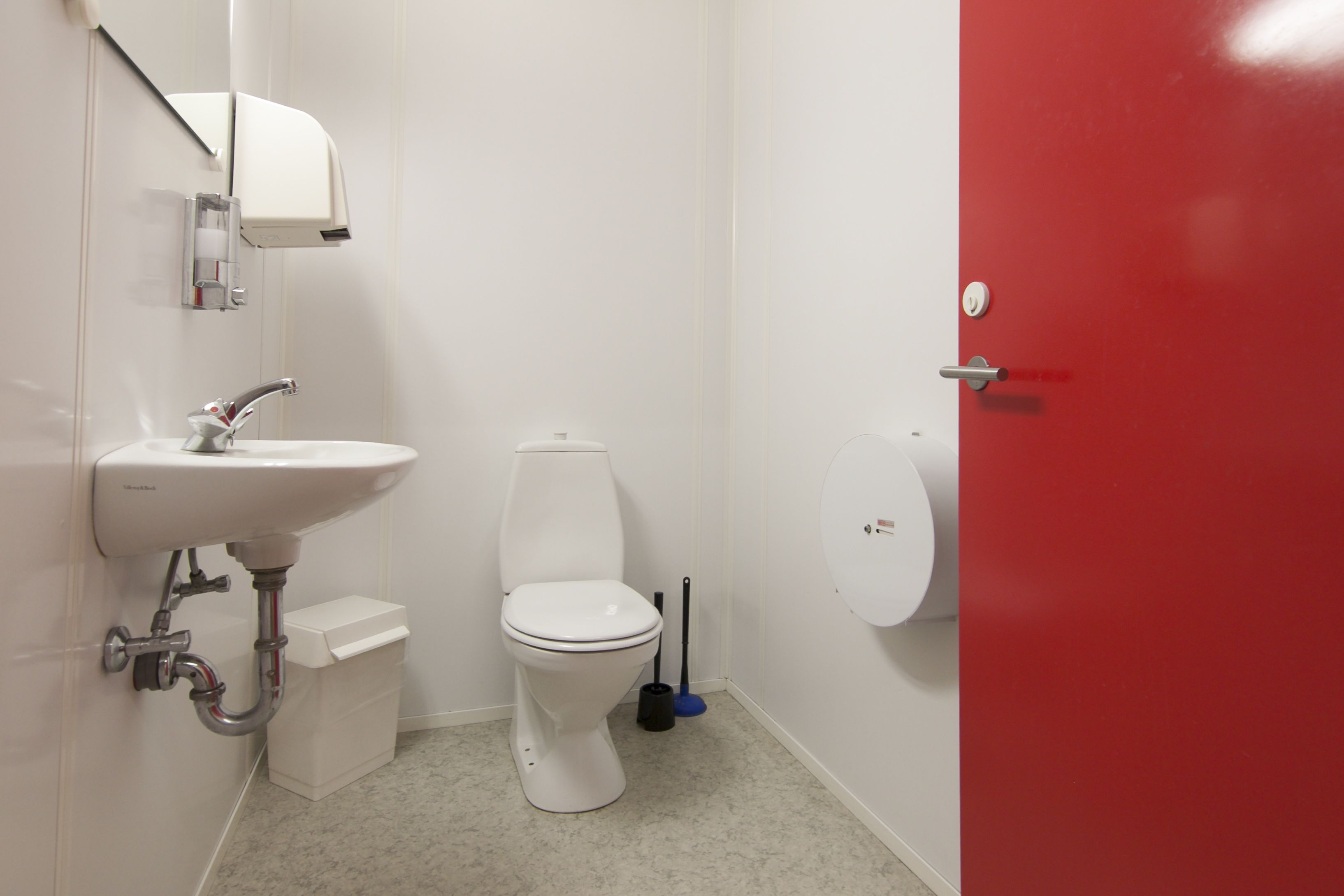A small bathroom with a white sink, toilet, and red door.