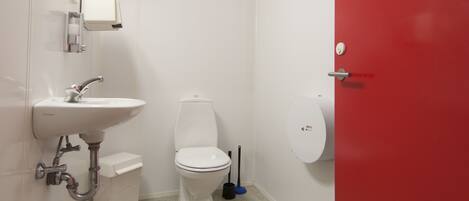 A small bathroom with a white sink, toilet, and red door.