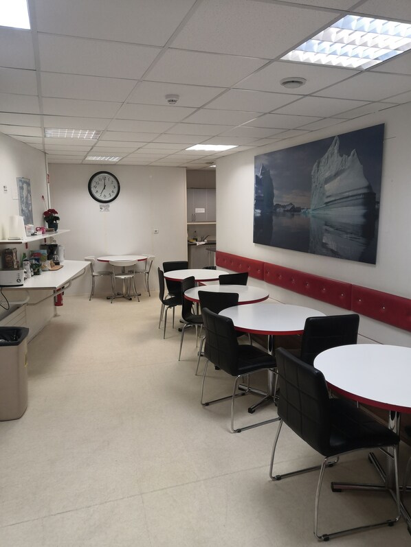 A conference room with white tables and black chairs, a clock on the wall, and a large painting of an iceberg.
