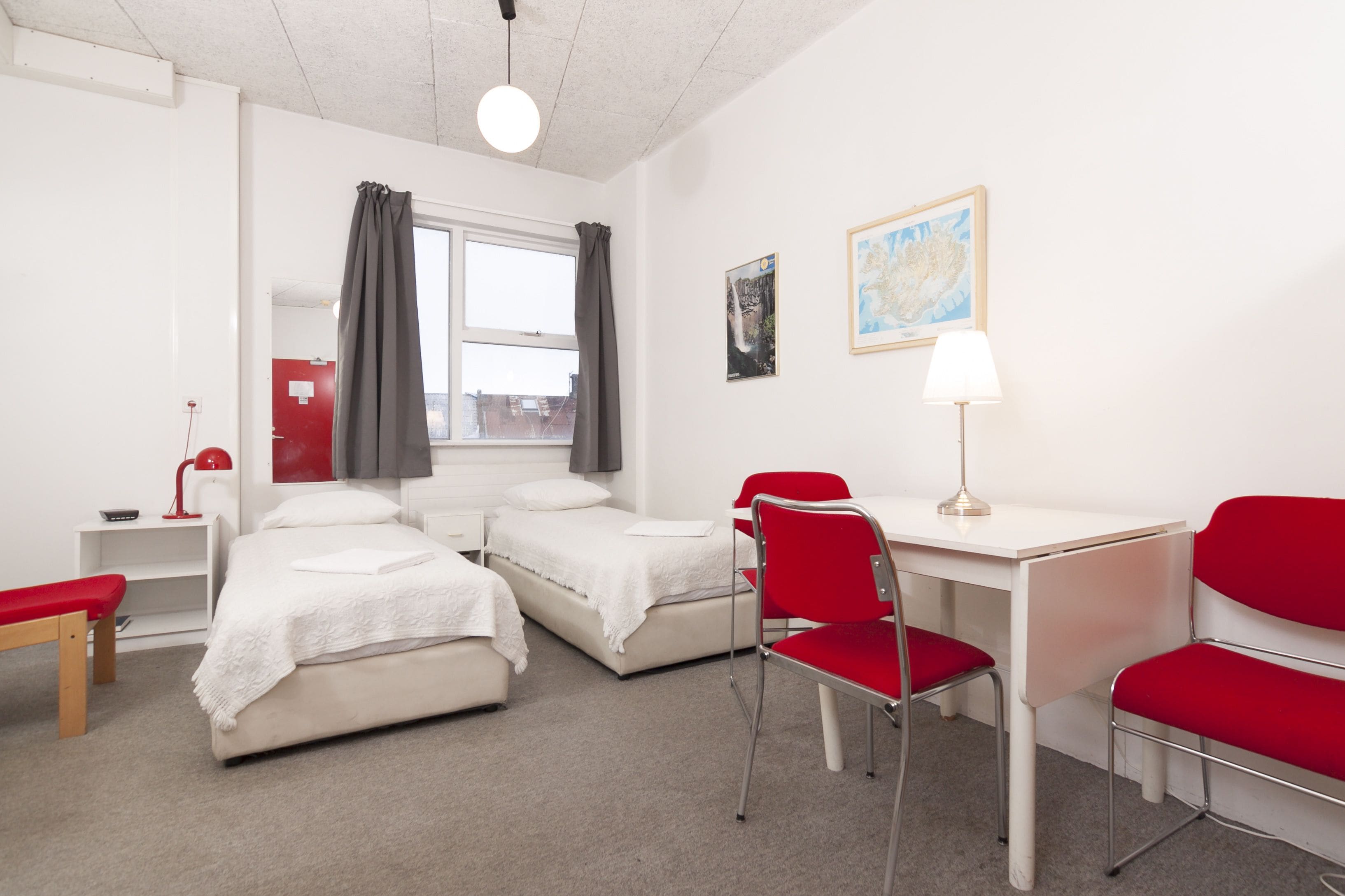A hotel room with two beds, a desk, a chair, a lamp, and a window with curtains.