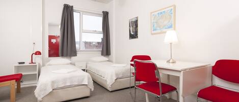 A hotel room with two beds, a desk, a chair, a lamp, and a window with curtains.
