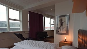 Habitación de hotel con dos camas, un escritorio, una silla, una lámpara y una ventana que da al aeropuerto.