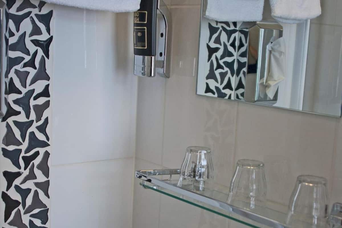 A bathroom with a white sink, a glass shelf with glasses, a towel rack with towels, and a shower curtain with a black and white pattern.