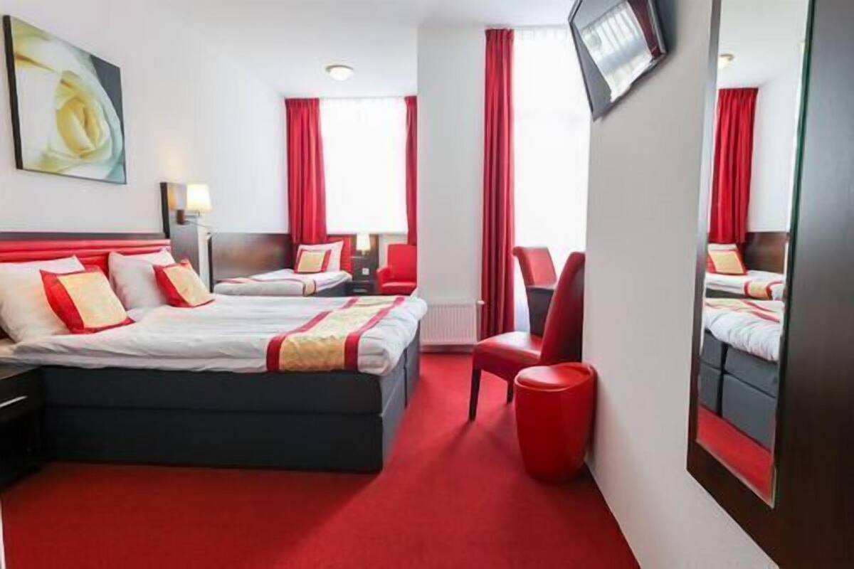 A hotel room with two beds, red curtains, a large mirror, and a red carpet.