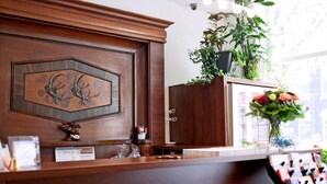 A reception desk with a wooden panel, a plant, and a vase of flowers.