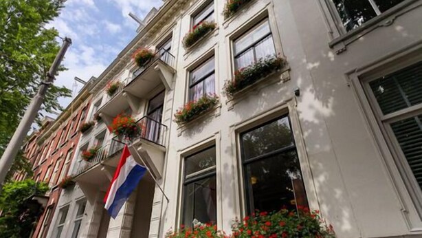 A row of white buildings with balconies adorned with flowers and a flag.