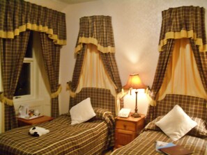 A hotel room with two beds, each with a canopy, a bedside table with a lamp, and a window with curtains. - Atholl Arms Hotel (Pitlochry)