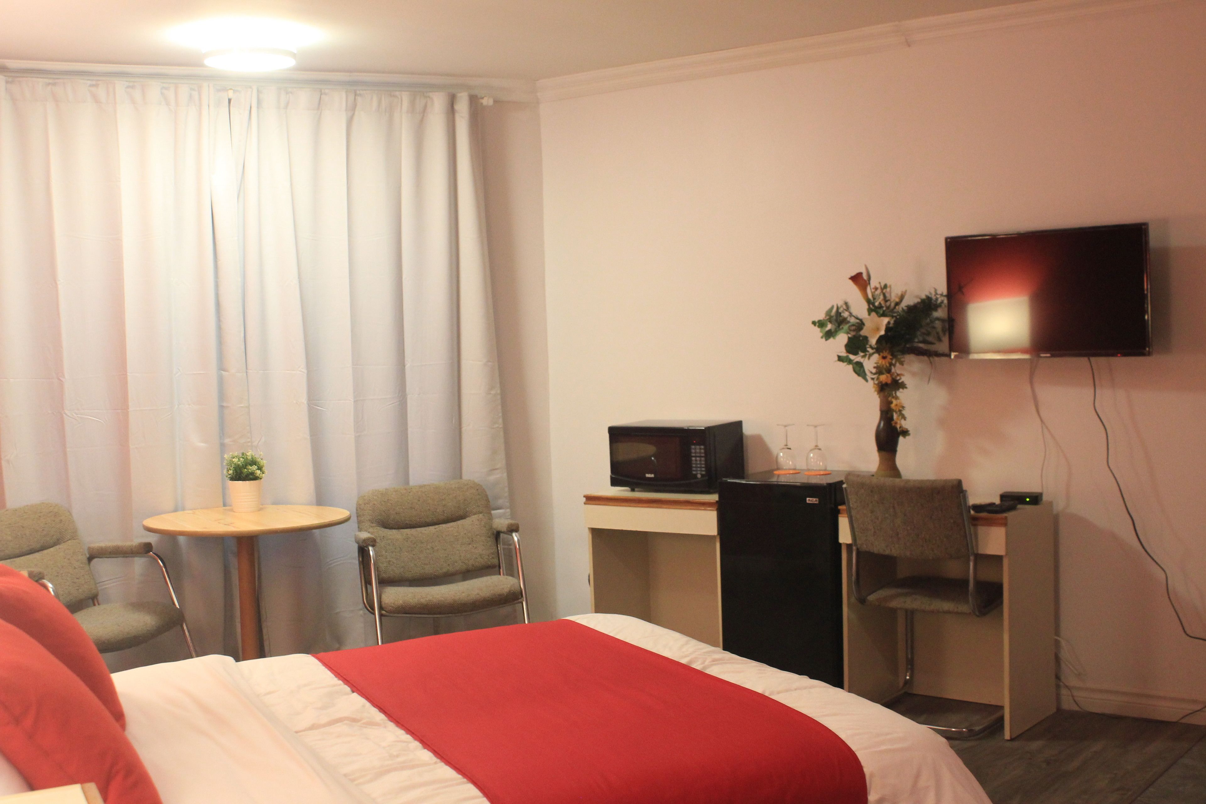 Une chambre d’hôtel avec un lit, un bureau avec un ordinateur, une télévision et deux chaises.