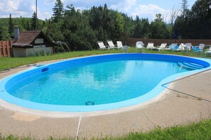 Ein Swimmingpool mit blauer Innenseite, umgeben von einer Betonplattform und weißen Liegestühlen.
