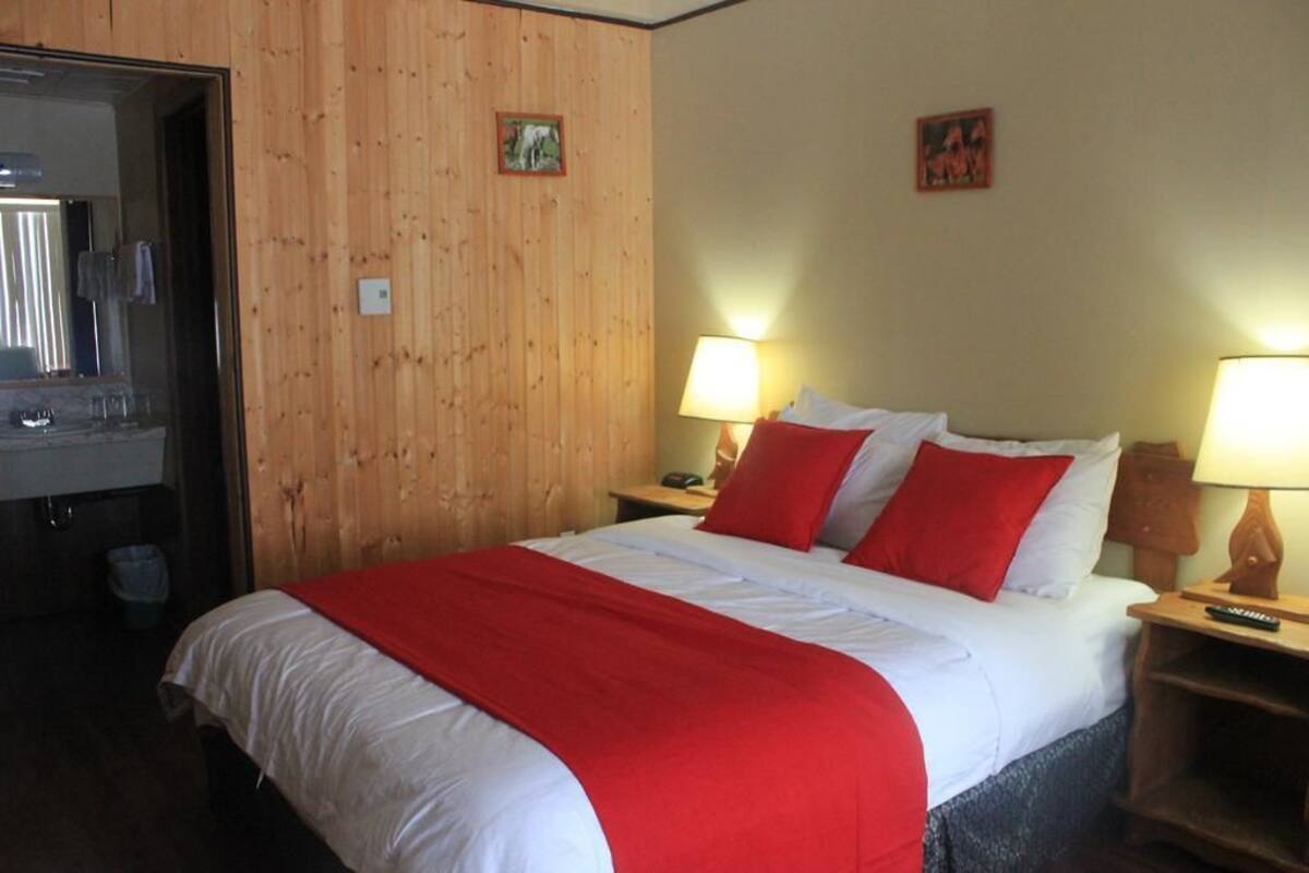 A hotel room with a wooden paneled wall, a bed with white and red bedding, two bedside lamps, and a mirror on the left.