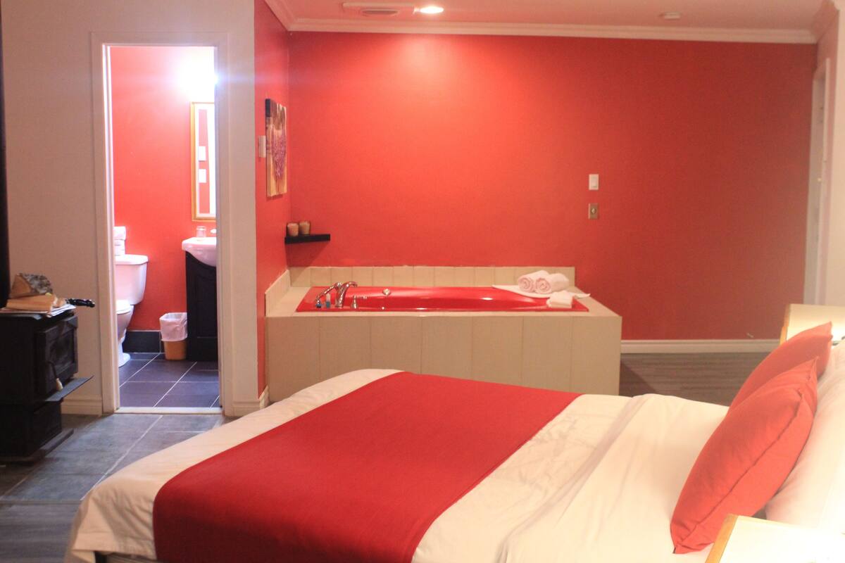 A hotel room with a bed, a red wall, a bathroom with a toilet and sink, and a bathtub.