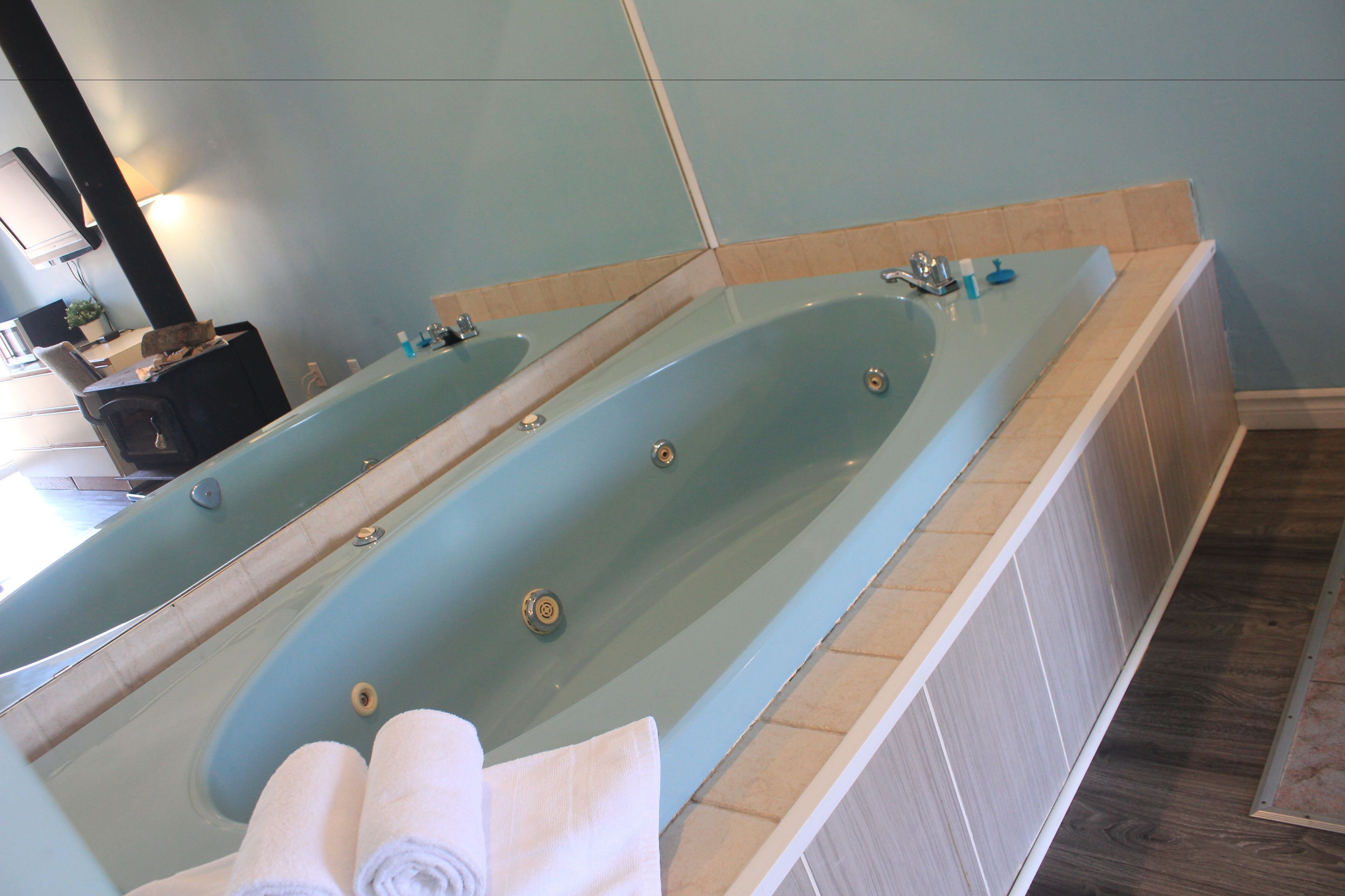 A large bathtub with a long mirror, a wooden floor, and a small sink area.