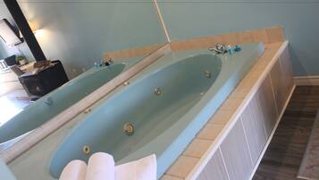 A large bathtub with a long mirror, a wooden floor, and a small sink area.