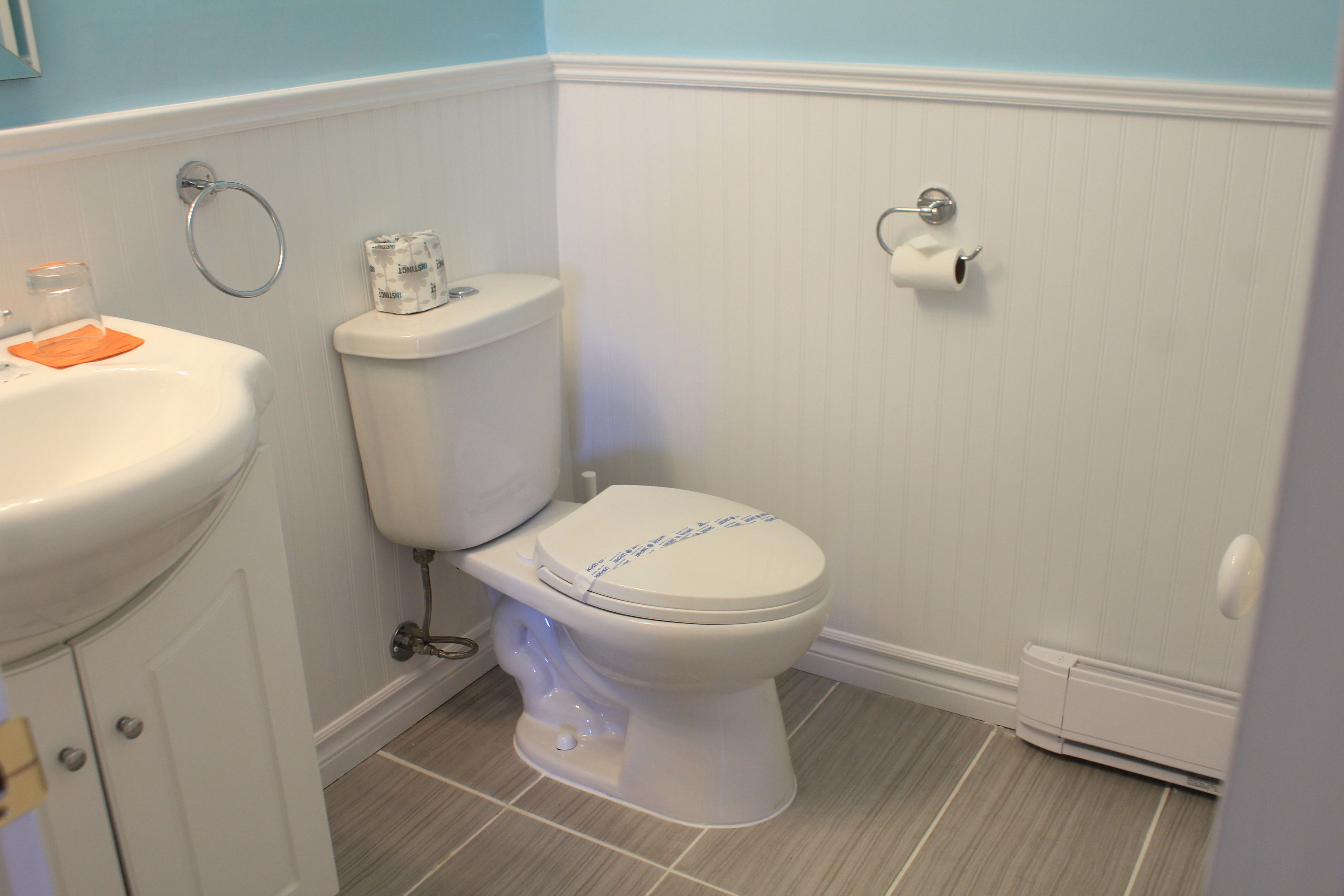 Baño con inodoro, lavamanos y suelo de baldosas blancas.