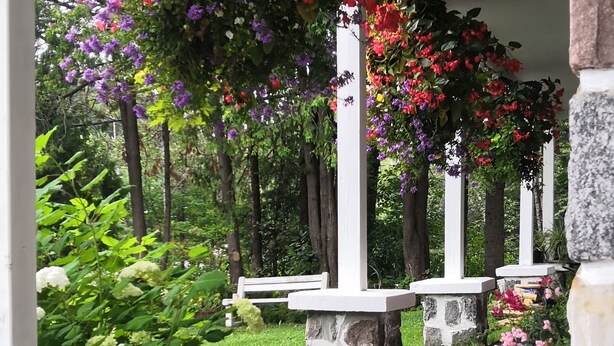 A covered walkway with stone benches and hanging floral arrangements. - Motel des Pays d'en Haut (Val David)
