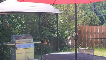 An outdoor patio with a metal table and chairs, a red umbrella, and a barbecue grill.