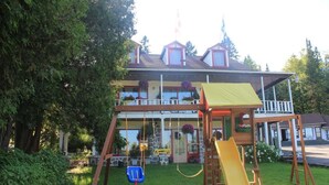 A two-story house with a wooden play structure in the yard, including a slide and swings. - Motel des Pays d'en Haut (Val David)