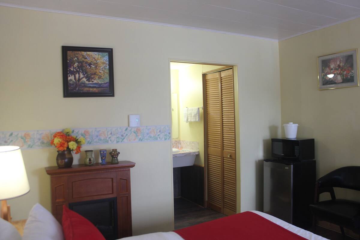A hotel room with a bed, a dresser, a microwave, a chair, and a bathroom visible through an open door.