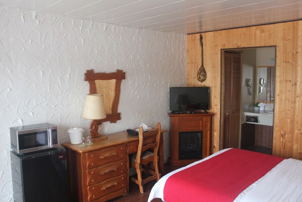 A hotel room with a bed, a television, a desk with a lamp, a microwave, and a refrigerator.